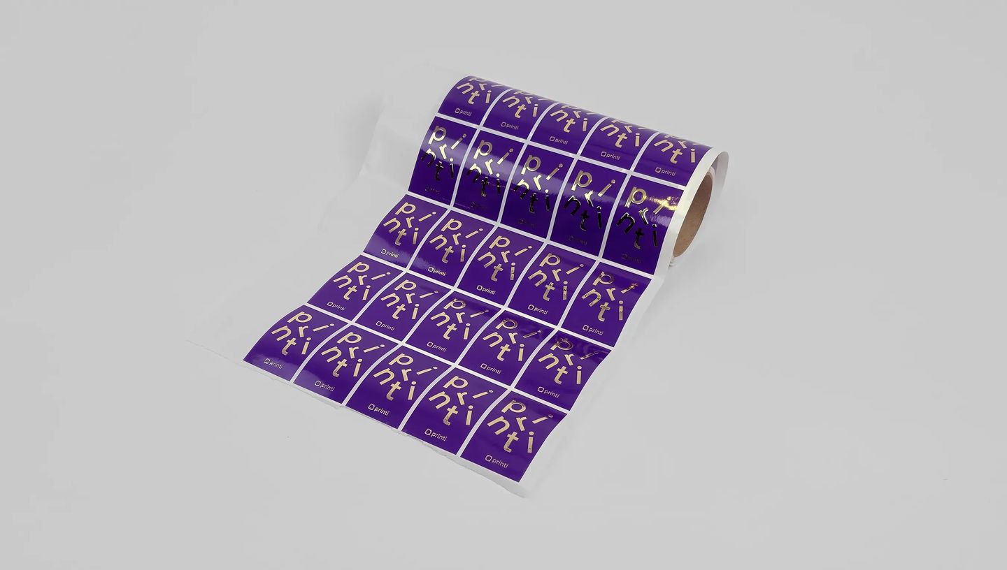 Adesivo retangular roxo em rolo com logotipo Printi em hot stamping dourado.