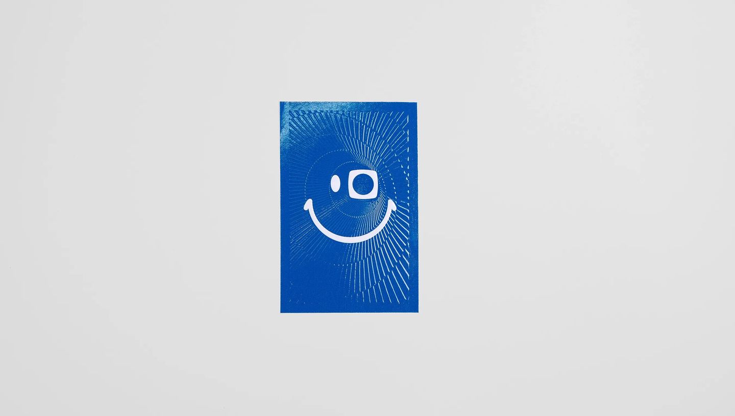 Adesivo retangular personalizado em fundo azul com acabamento brilhante e ilustração gráfica branca em formato de rosto sorridente, utilizado para rotulagem de produtos, embalagens, brindes e comunicação visual de marcas.