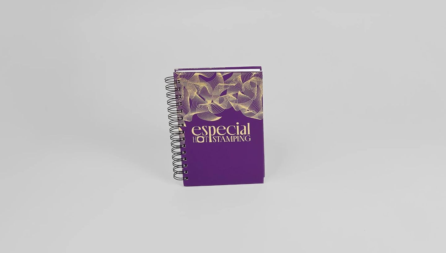 Agenda personalizada com capa roxa, detalhes em hot stamping dourado e encadernação espiral metálica.