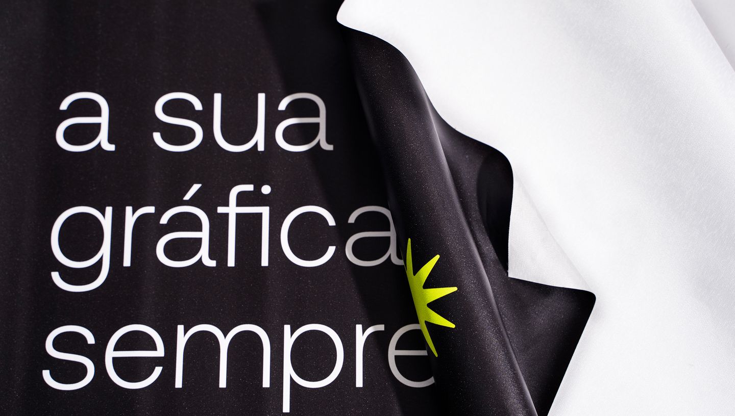 Detalhe de tecido de bandeira personalizada com impressão em alta definição e verso branco, destacando a frase 'a sua gráfica, sempre