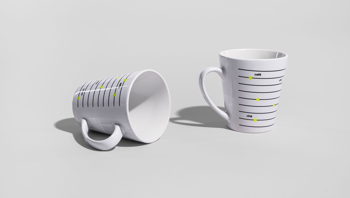 Caneca inclinada e outra de pé sobre fundo cinza, com design gráfico de linhas pretas e pontos verdes, exibida em fundo neutro