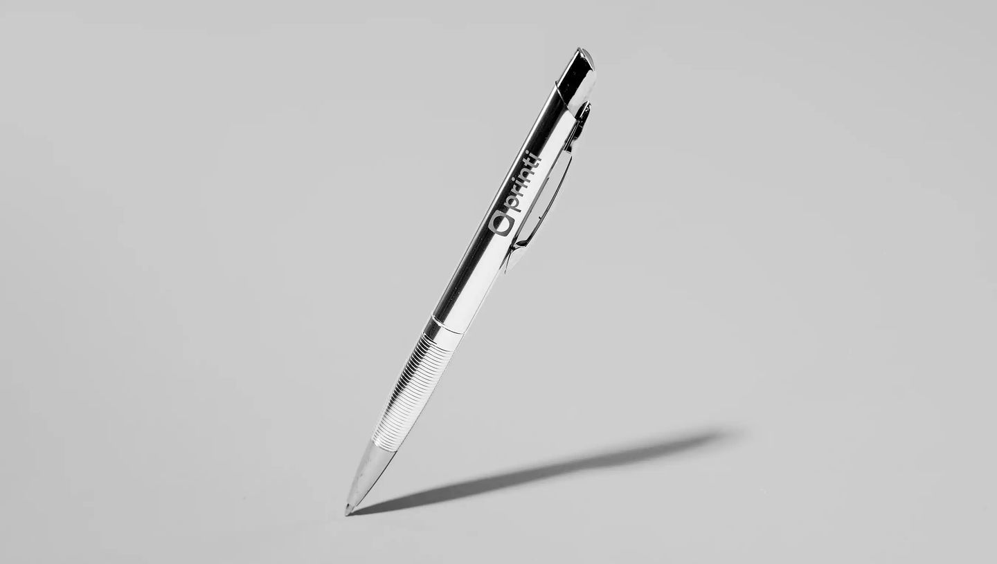 Caneta metálica personalizada prateada com logo Printi gravado, design moderno com acabamento brilhante e área texturizada para pegada, ideal para brindes corporativos, eventos empresariais, kits institucionais e ações promocionais de marca.