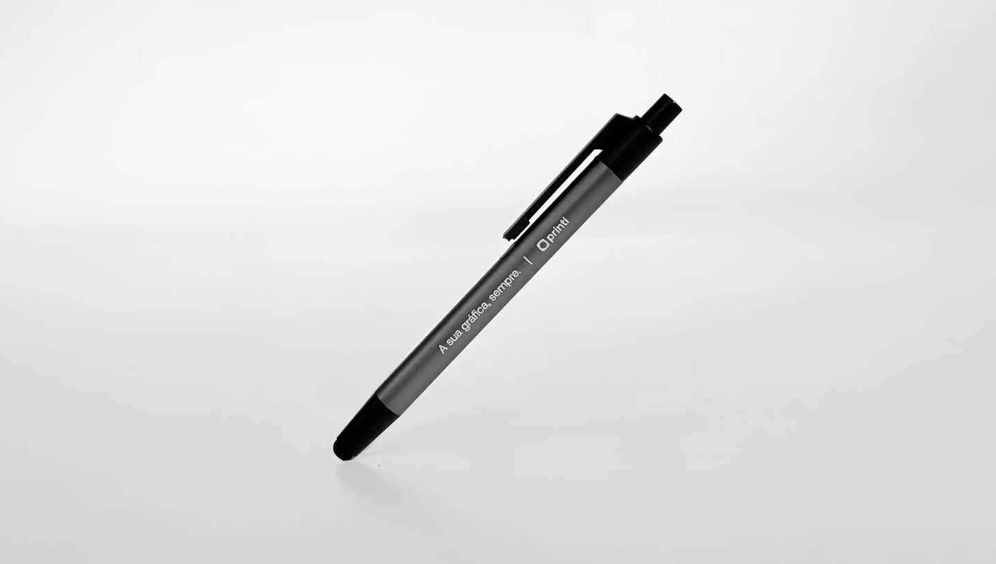 Caneta metálica personalizada com acabamento cinza e detalhes pretos, exibindo o logo da Printi e a frase “A sua gráfica, sempre.” gravados no corpo da caneta, apresentada em fundo neutro para destacar o design elegante e o uso como brinde corporativo ou 