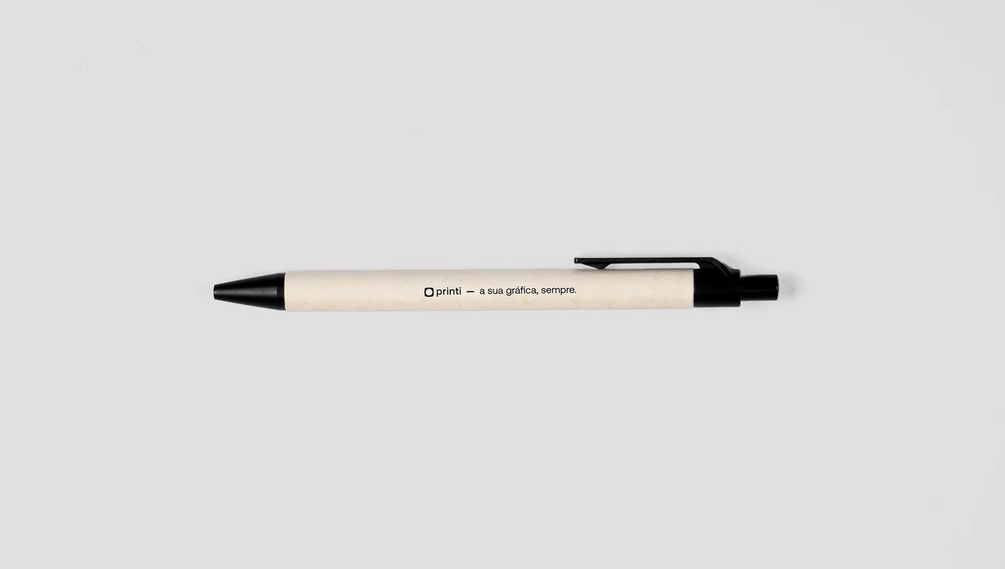Caneta personalizada horizontal com corpo bege e detalhes pretos, com impressão “printi — a sua gráfica, sempre”, sobre fundo cinza claro.