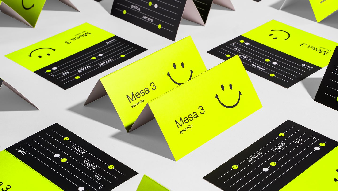 Cartões de mesa personalizados dispostos sobre superfície branca, com design vibrante em preto e amarelo neon, texto “Mesa 3, aproveite!” e ícone de carinha sorridente.