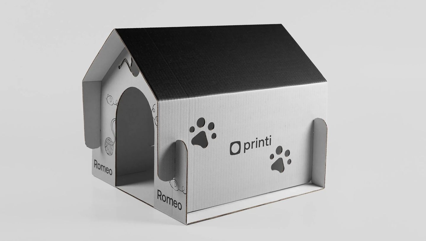 Casa de Gato de Papelão personalizada com telhado preto, ilustrações de patinhas e o nome 'Romeo' em layout funcional e minimalista.