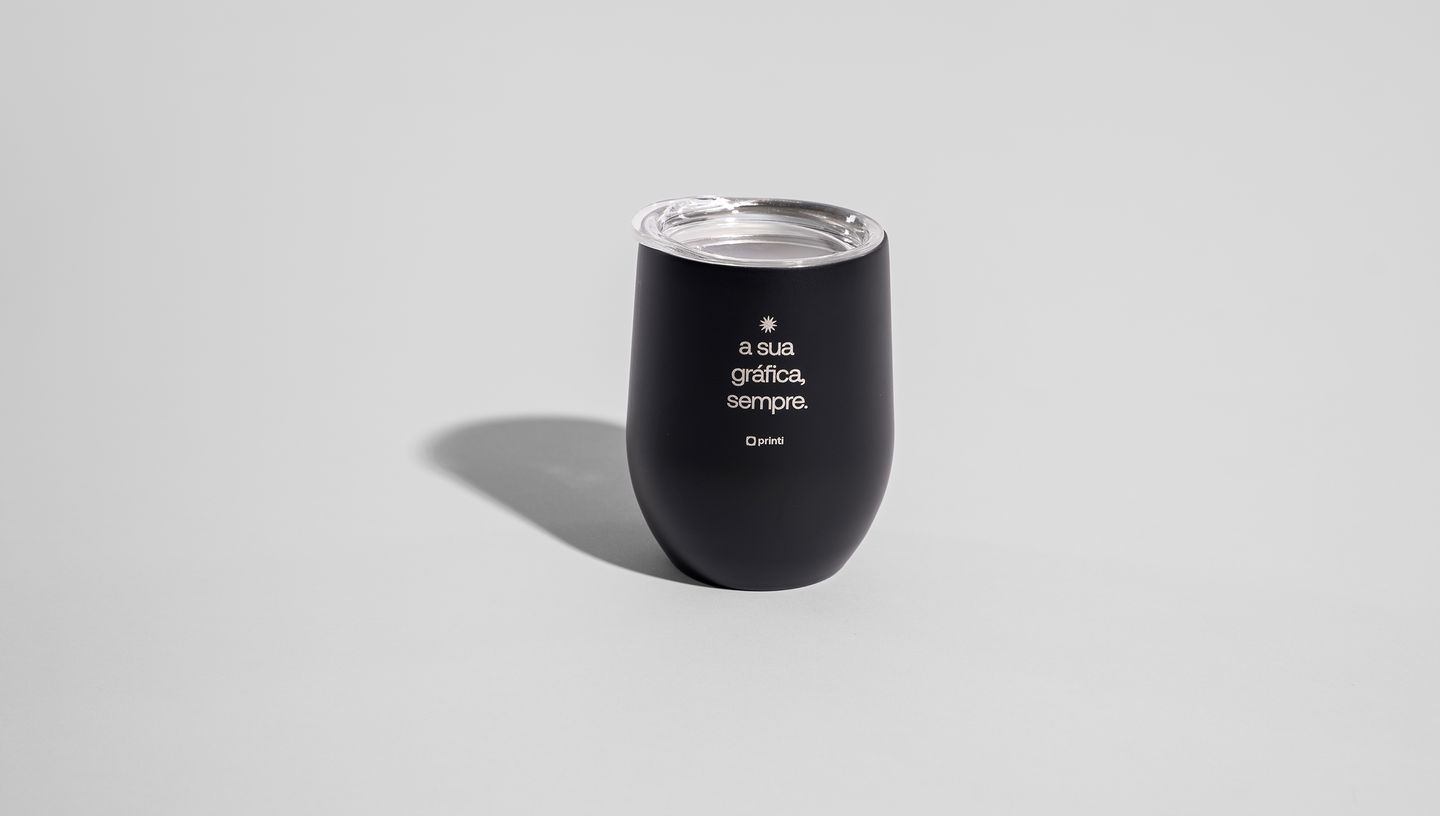 Copo Térmico de 400 ml preto com tampa, apoiadao em superfície lisa e branca, com logo e frase personalizada dizendo "a sua gráfica sempre"