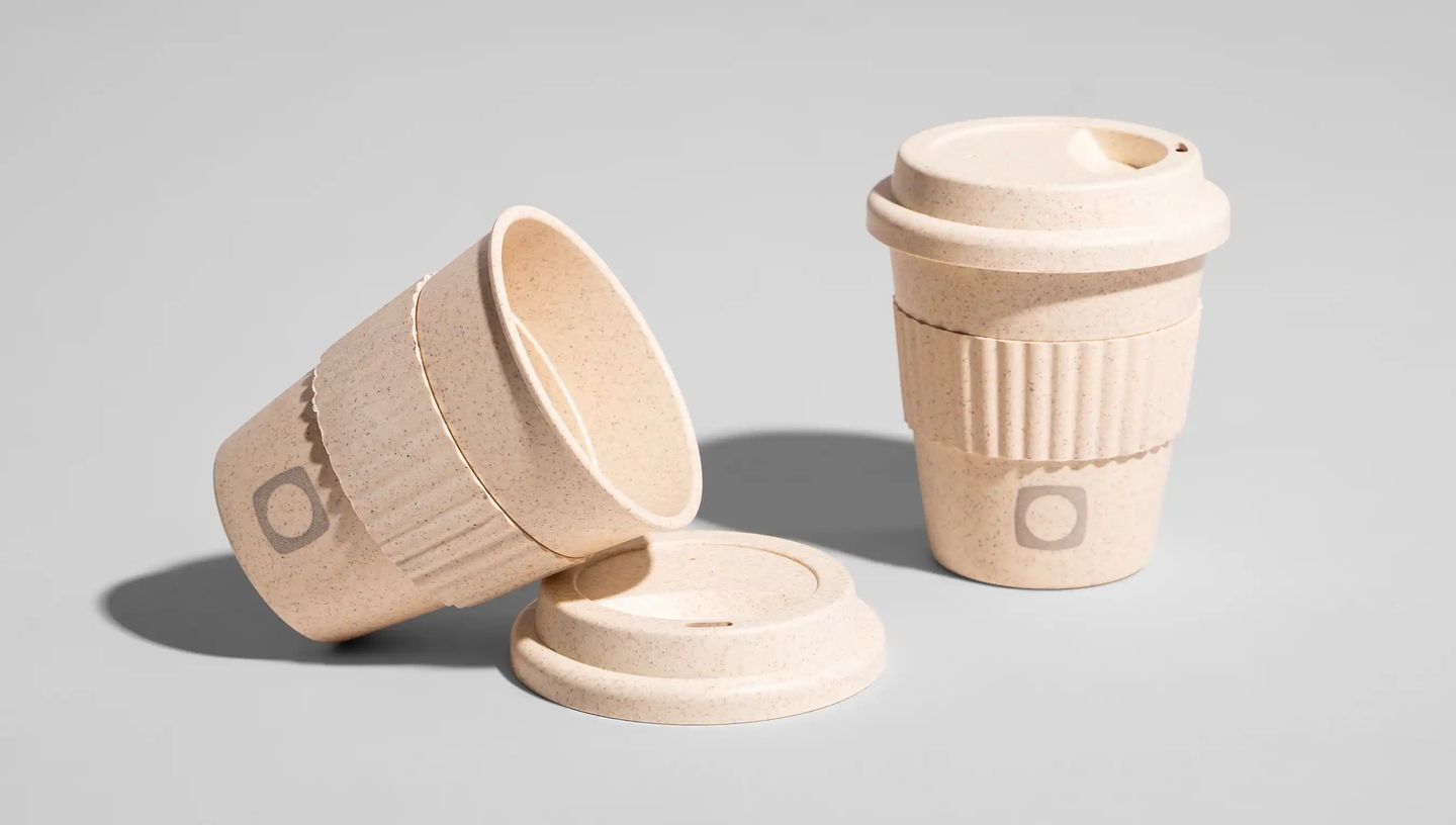 Copo para viagem personalizado de 380ml em tom bege, com tampa e pegador, sendo um copo exibido deitado e o outro em pé em fundo liso e branco.