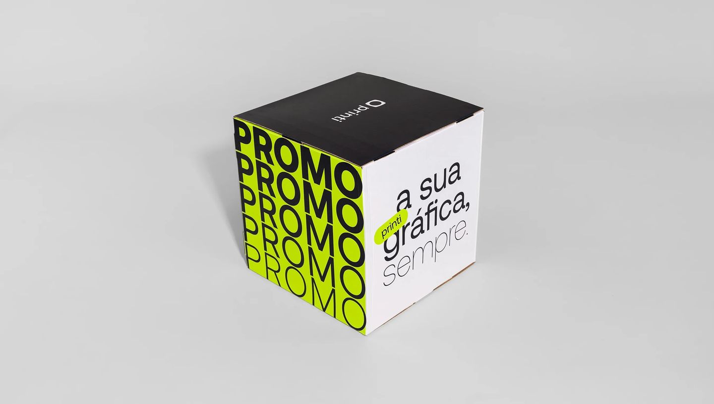 Cubo de papelão montado com layout contendo estampas mostrando a logo da Printi, palavra "promo" e a frase "printi, sua gráfica sempre"