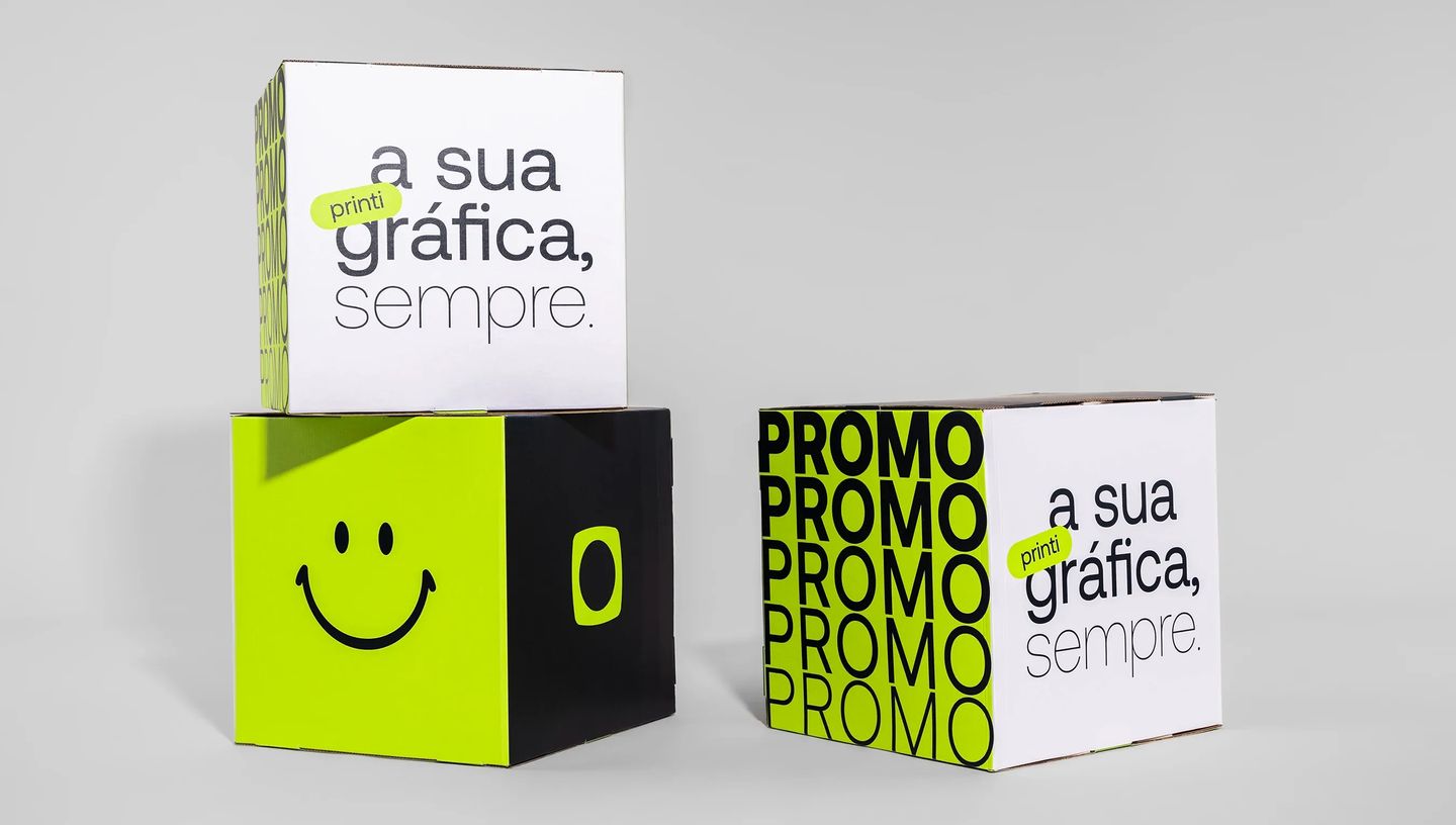 Dois cubos montados um em cima do outro e outro cubo montado e posicionado ao lado dos dois, com design promocional vibrante, estampados com frase dizendo "printi, a sua gráfica, sempre", logotipo da printi, smile e palavra 'PROMO'.
