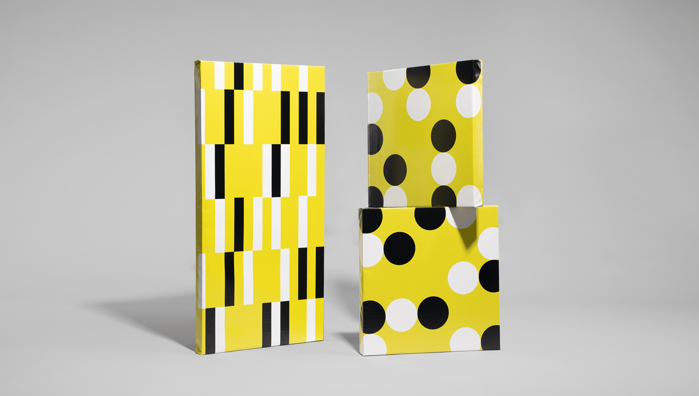 Três modelos de banner com moldura em painel rígido expostos em pé sobre fundo cinza. À esquerda, o banner apresenta uma estampa geométrica com listras verticais em preto, branco e amarelo vibrante, criando um efeito visual moderno e dinâmico. À direita, 