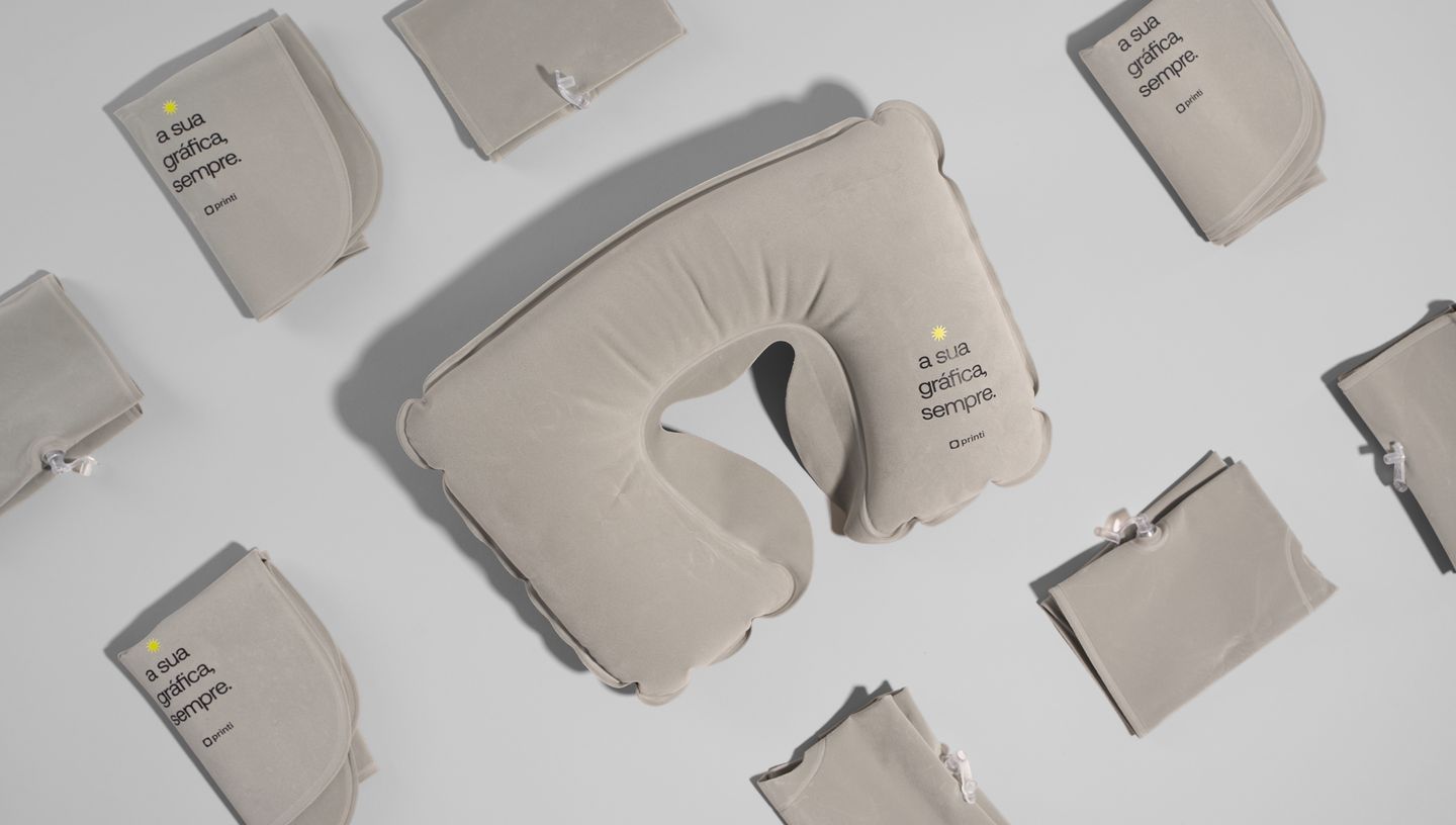 Almofada de pescoço inflável personalizada com a frase “a sua gráfica, sempre” da Printi, acompanhada de estojos individuais dobráveis 