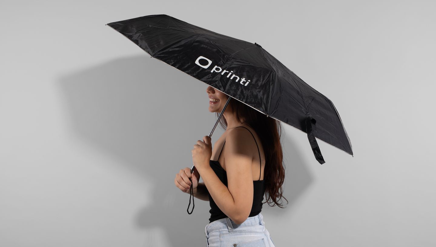 Mulher segurando guarda-chuva dobrável aberto na cor preta com a logo da Printi