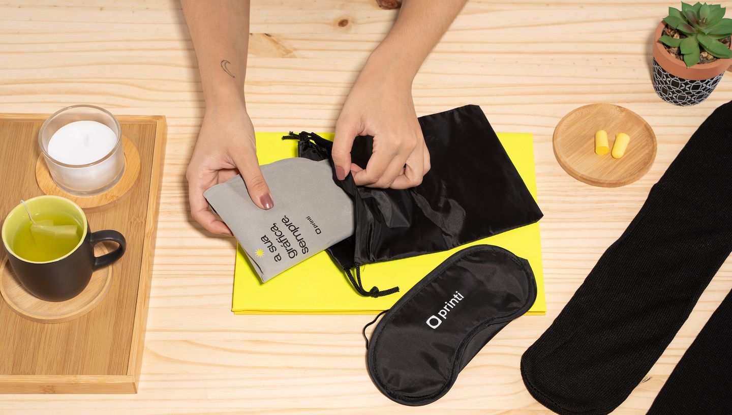 Pessoa colocando lenço dentro de bolsa do kit de viagem ao lado de máscara para dormir e itens de decoração