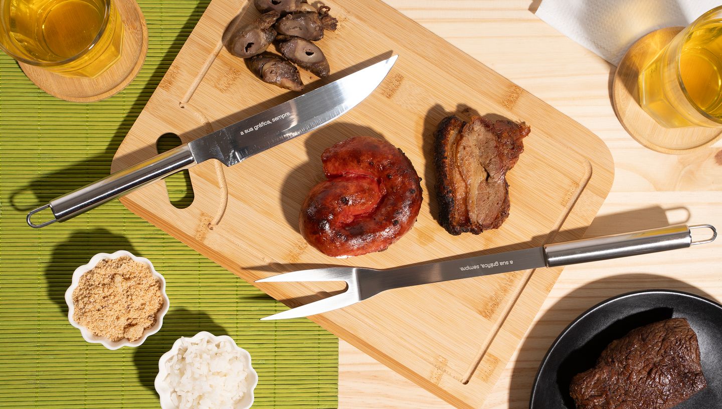 Garfo e faca do kit churrasco em tábua de madeira com comida ao redor