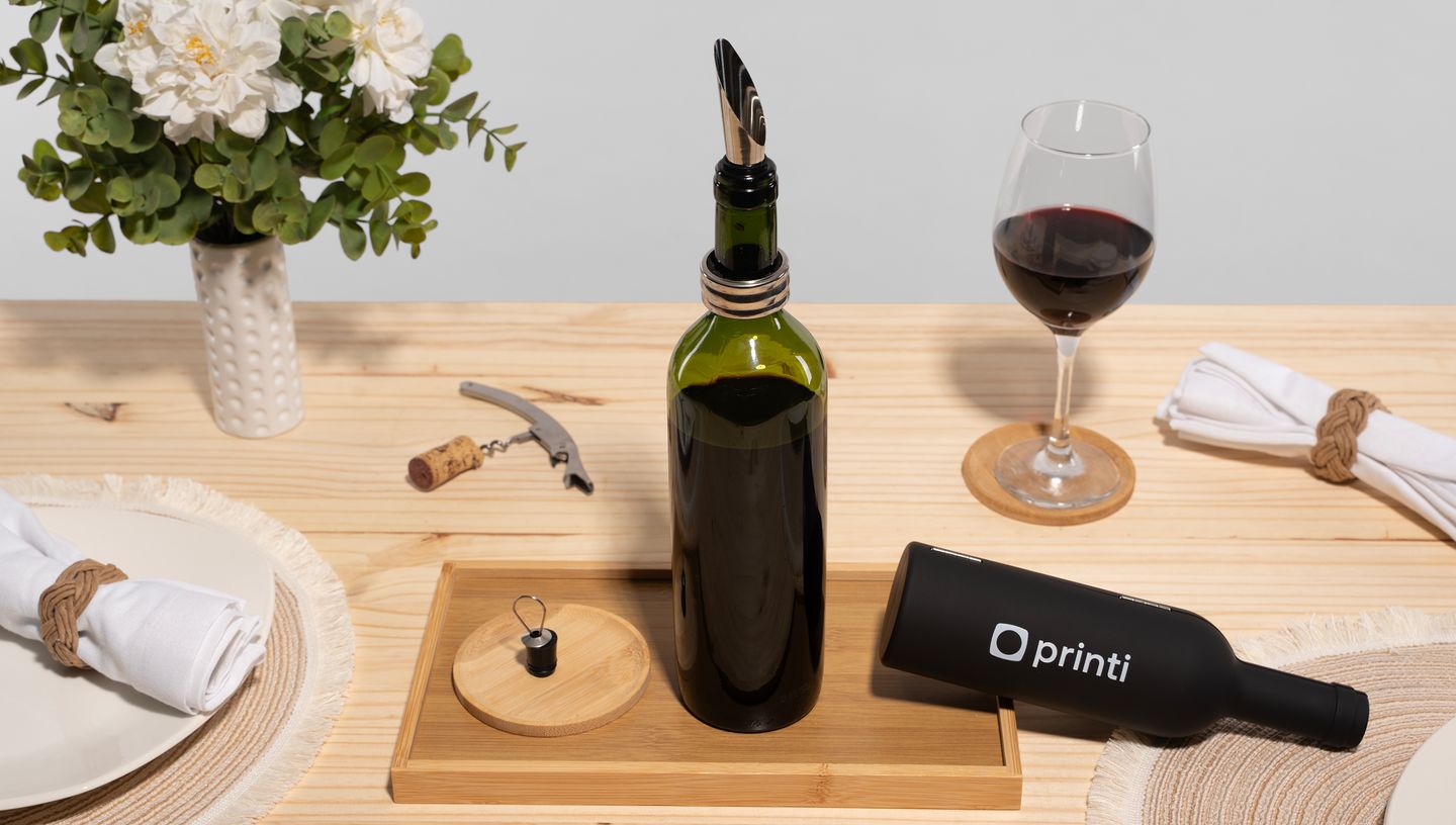Conjunto para vinho em metal com garrafas de vinho, taça, vaso de planta e utensílios de madeira ao redor.