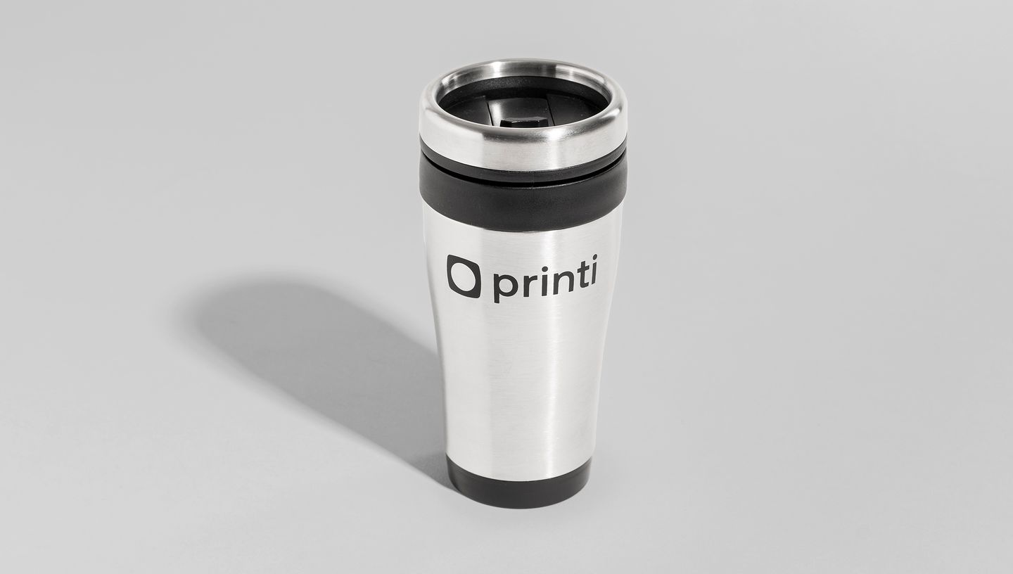 Copo térmico de inox posicionado em pé sobre superfície cinza neutra, com logotipo da Printi em destaque e tampa com bico dosador