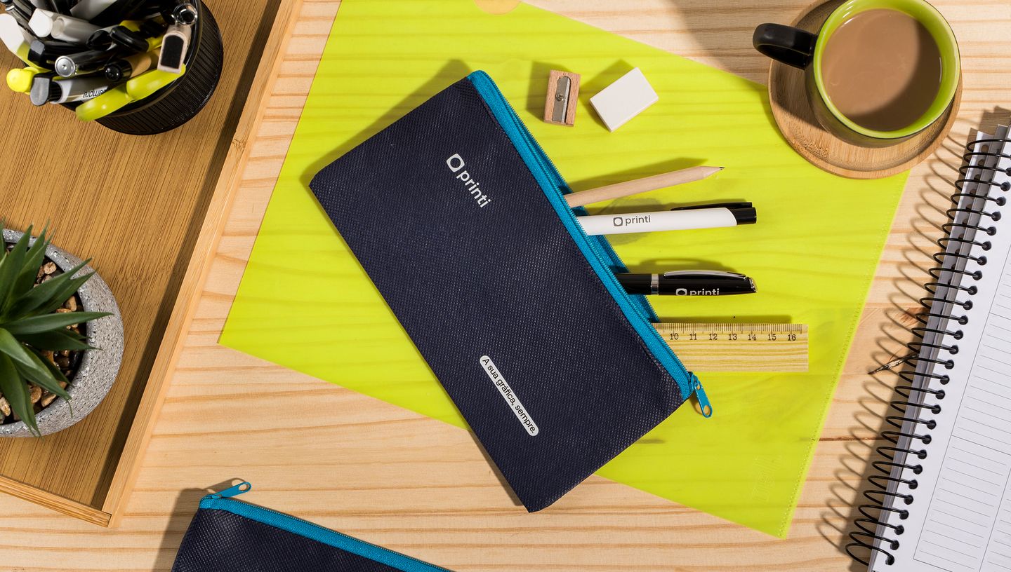 Estojo simples nas cores azul claro e escuro, com material escolar ao redor e xícara de café.