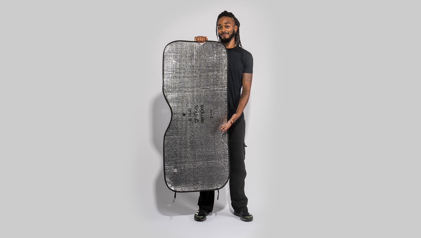 Pessoa segurando um protetor solar prateado para carro, com textura refletiva e formato curvado, ideal para cobrir o para-brisa.