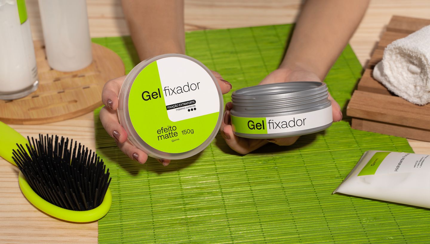 Pote de gel com rótulo personalizado em toalha verde com escova e produtos para cabelo sobre mesa de madeira.