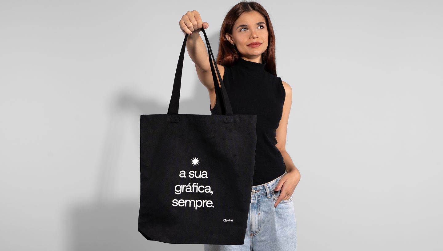 Mulher segurando uma ecobag preta de algodão reciclado com o slogan da Printi.