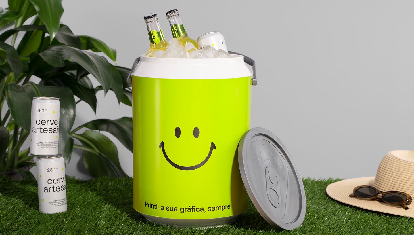 Cooler personalizado verde em cima de grama e com garrafa de cerveja e gelo dentro, com latas de cerveja e chapéu ao redor.