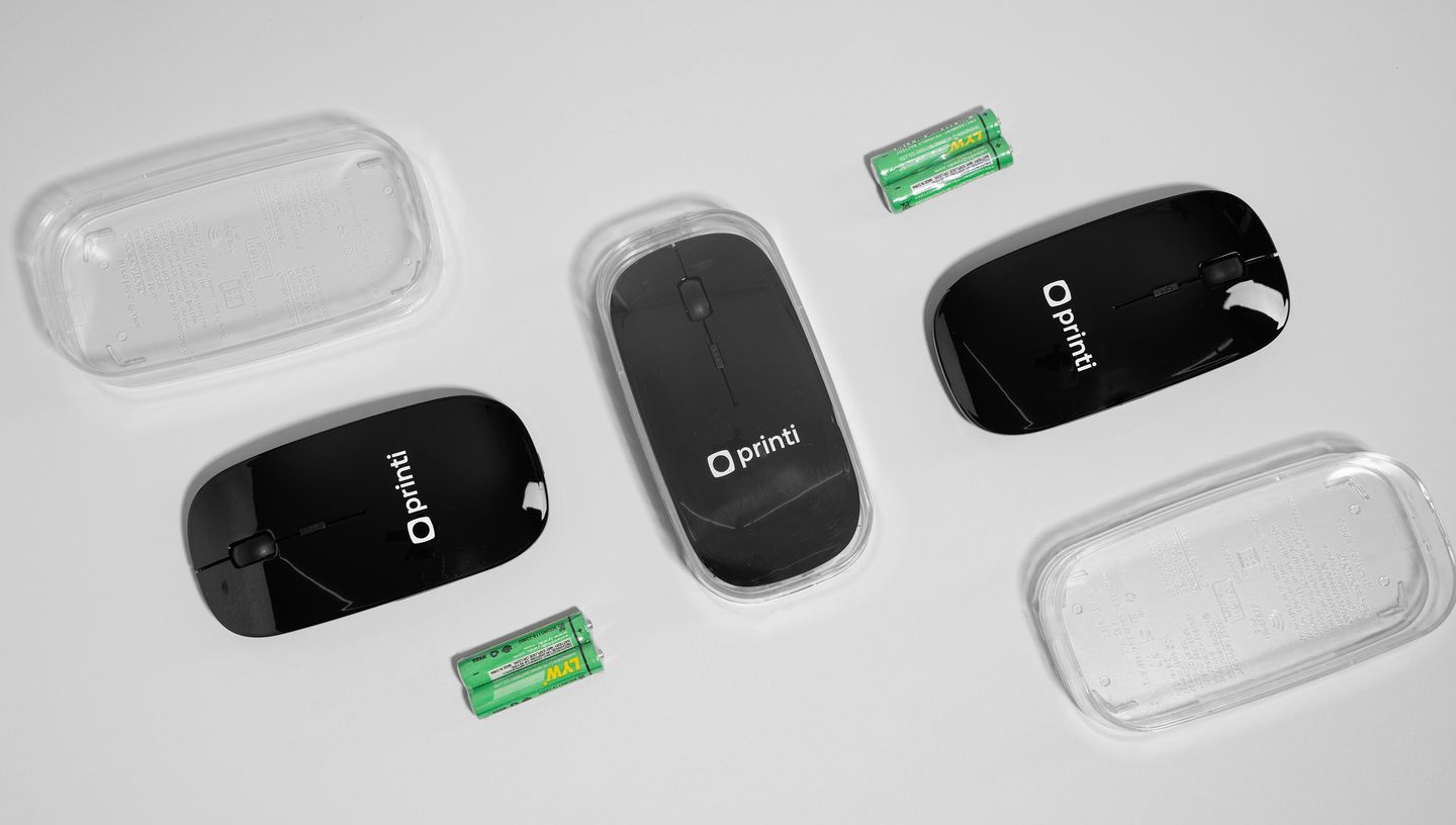 Mouse sem fio personalizado na cor preta com logo da Printi ao lado de pilhas e capa para mouse..