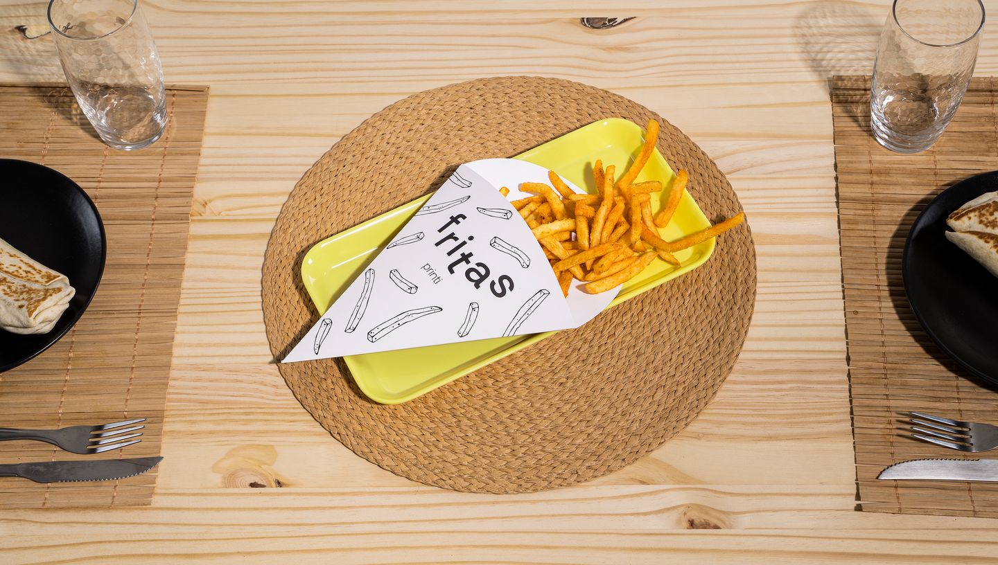 Embalagem cone personalizada para fritas sobre prato amarelo, com design ilustrado e palavra "fritas" impressa em preto
