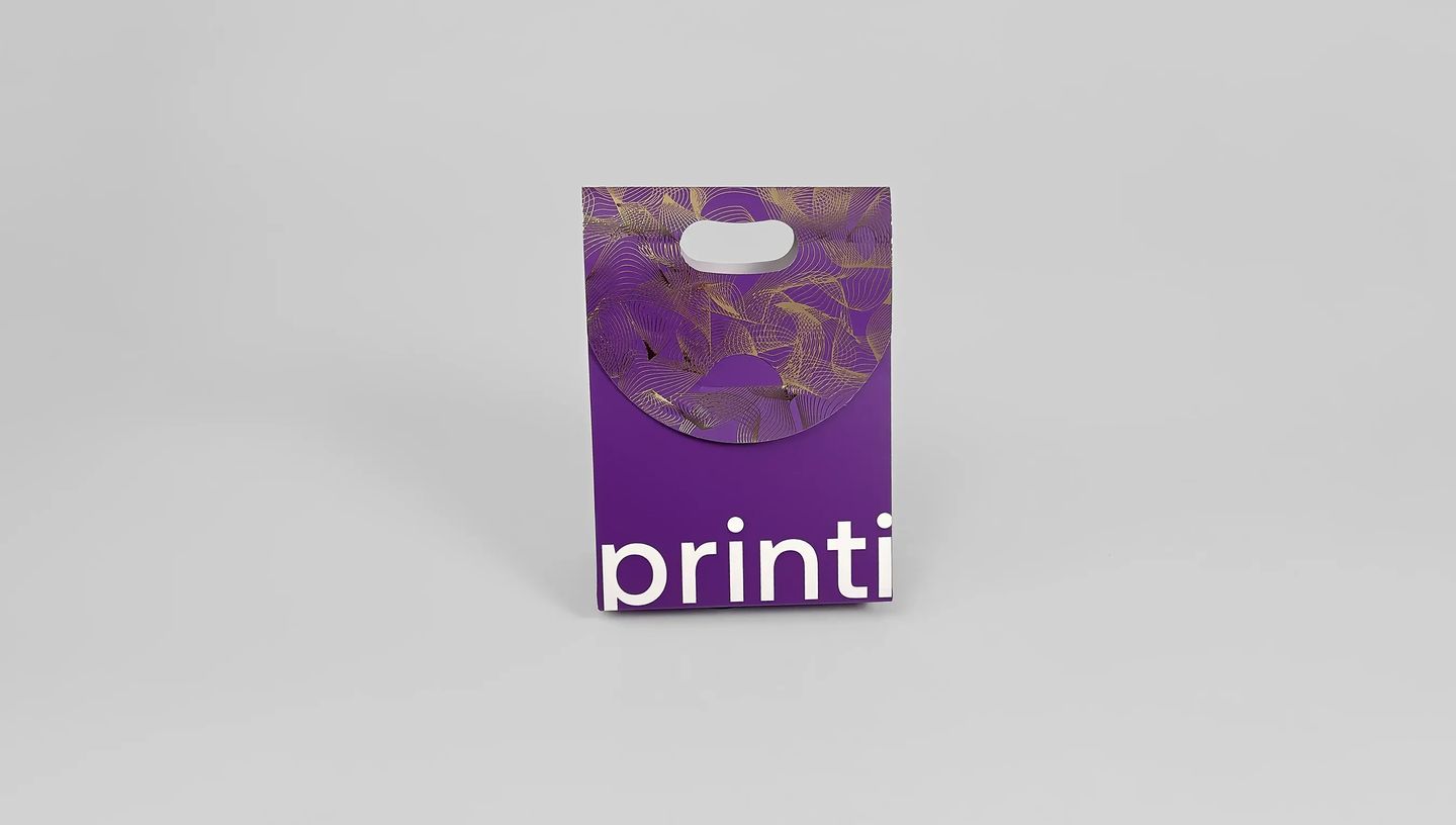 Vista frontal de embalagem tipo sacola roxa personalizada com logotipo Printi e detalhes dourados.