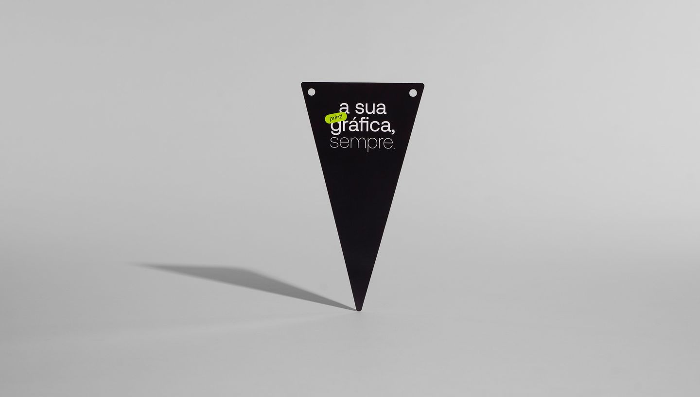 Bandeirola preta personalizada com a frase 'printi, a sua gráfica sempre' e furos superiores para fixação em cordão ou estrutura