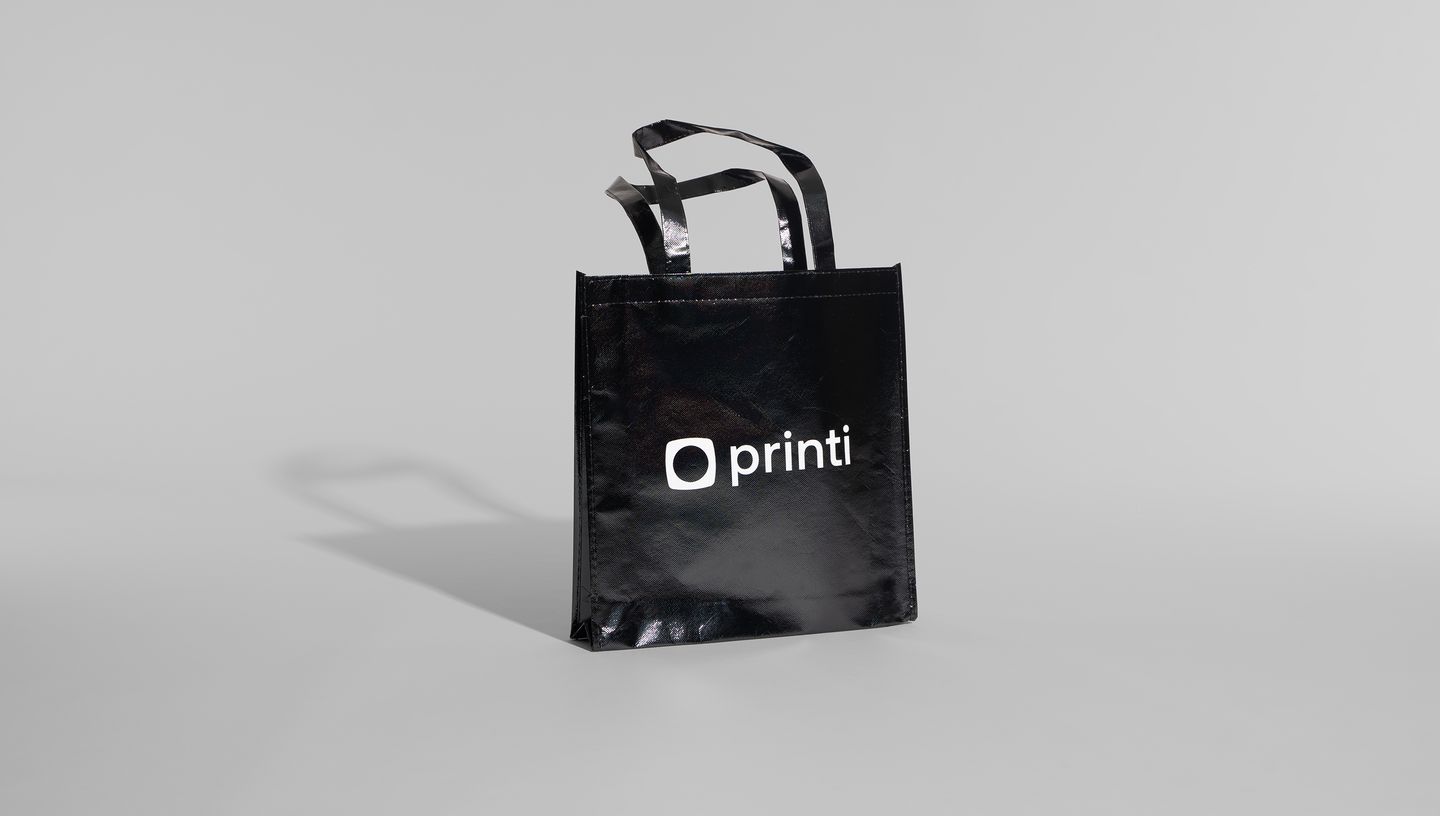 Imagem de sacola em TNT Laminado preta com logo da Printi em fundo cinza
