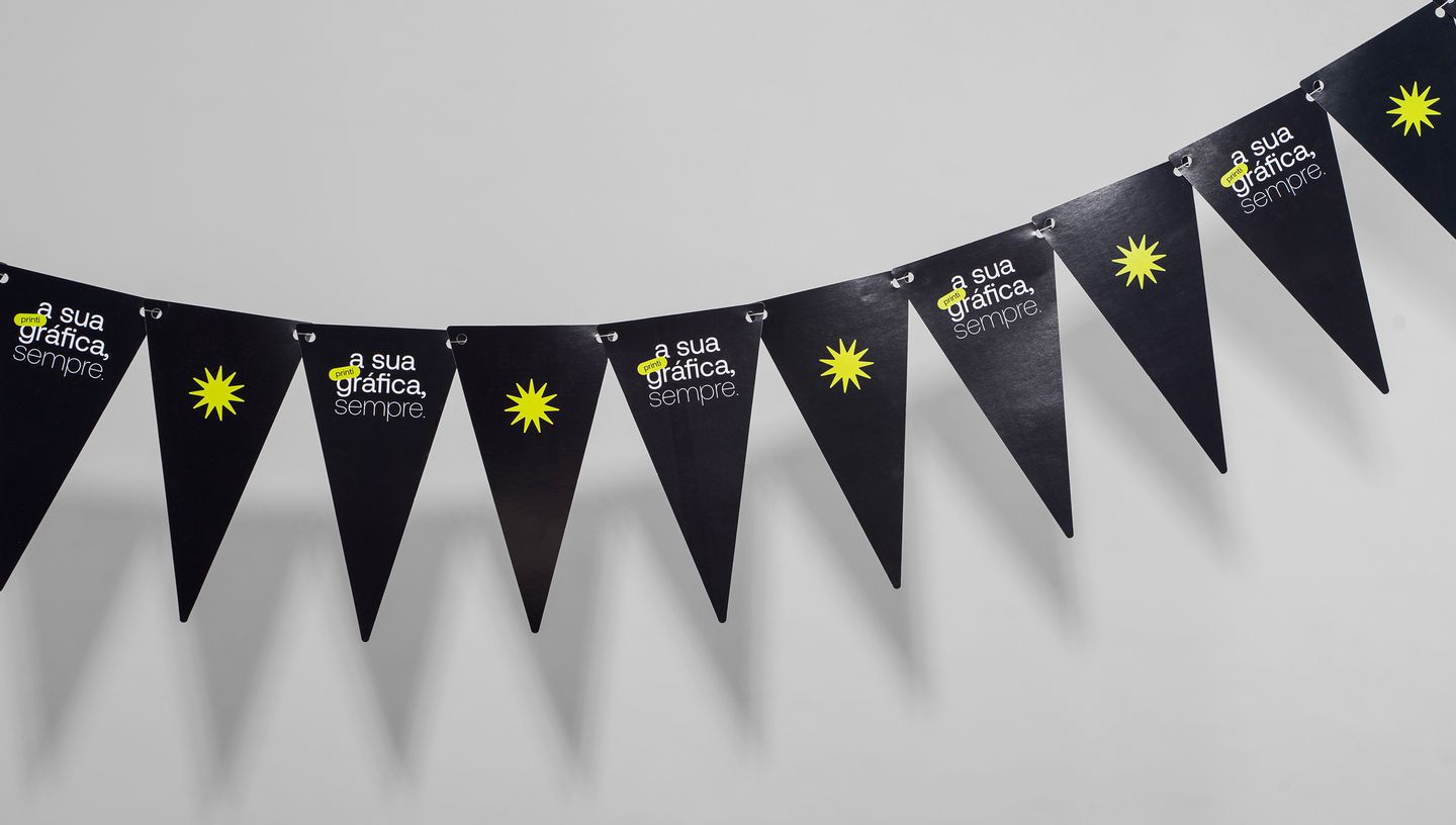 Cordão com várias bandeirolas pretas personalizadas com a frase 'printi, a sua gráfica sempre' e ícone gráfico amarelo