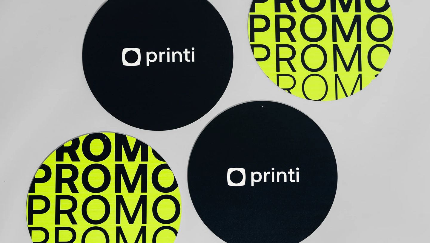 Conjunto de placas circulares personalizadas com design moderno da Printi, em fundo preto com logotipo branco e versões em verde-limão com tipografia “PROMO”, utilizadas como materiais de comunicação visual e sinalização promocional para eventos, campanha