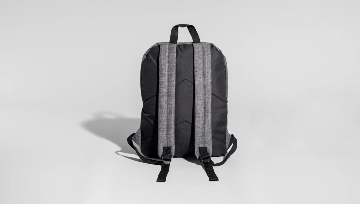 Mochila para notebook personalizada da Printi exibida pela parte traseira, com alças acolchoadas e design ergonômico em tecido cinza e preto sobre fundo neutro