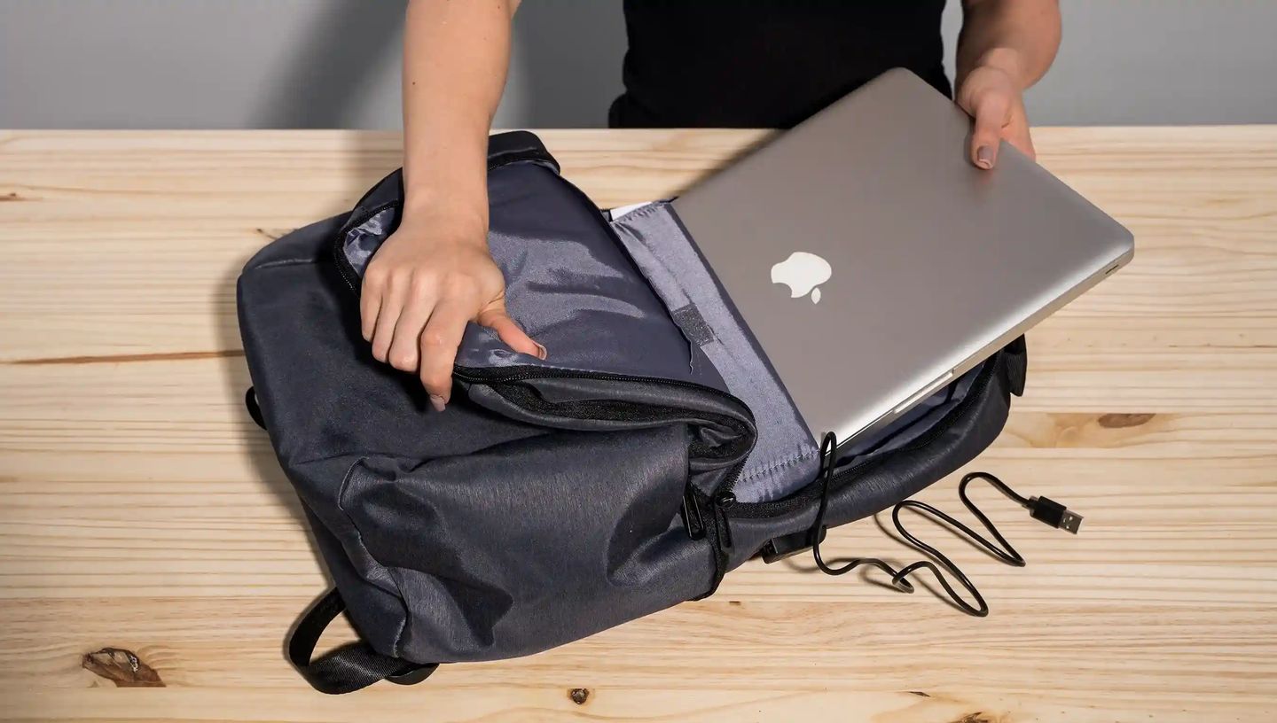 Pessoa colocando notebook em mochila para notebook personalizada da Printi com compartimento acolchoado e porta USB externo