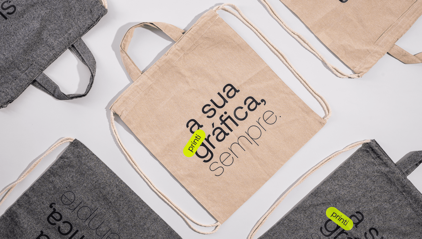 Mochilas saco personalizadas em algodão reciclado nas cores bege e cinza com estampa “a sua gráfica, sempre.” da Printi