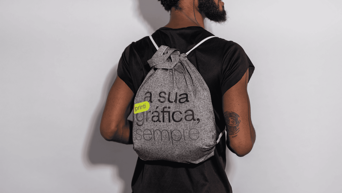 Homem usando mochila saco personalizada em algodão reciclado cinza com estampa “a sua gráfica, sempre.” da Printi