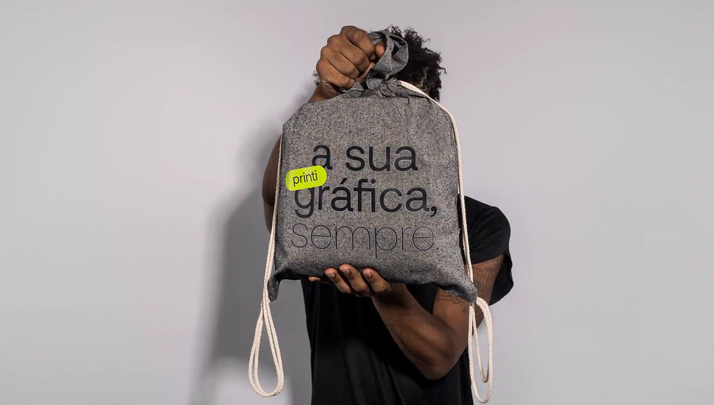 Pessoa segurando mochila saco personalizada em algodão reciclado cinza com estampa “a sua gráfica, sempre.” da Printi