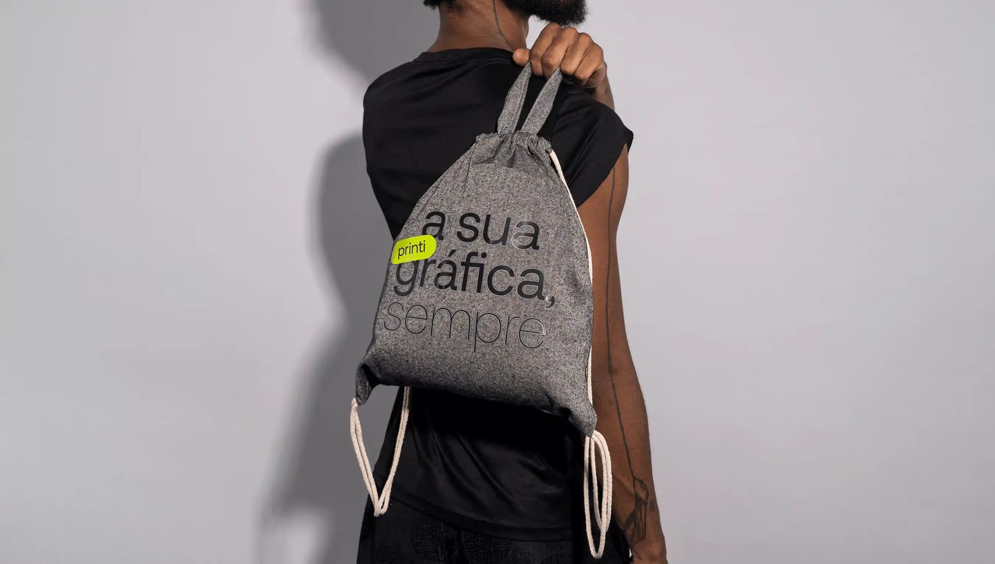 Homem usando mochila saco personalizada em algodão reciclado cinza com estampa “a sua gráfica, sempre.” da Printi