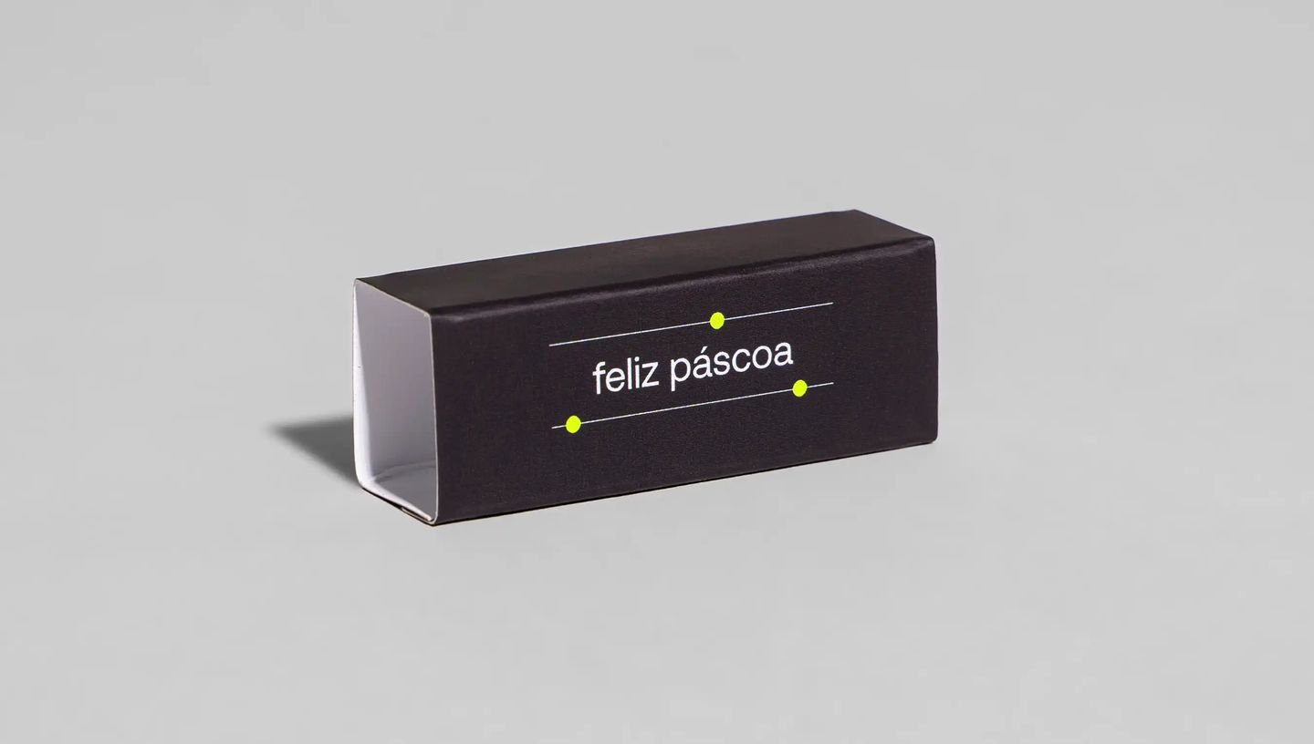 Rótulo de Bis preto com acabamento brilhante, frase “feliz páscoa” centralizada e pontos amarelos decorativos