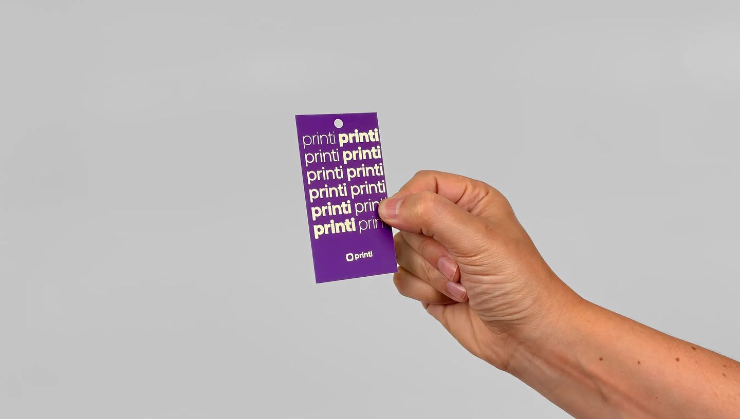 Tag personalizada retangular com furo para pendurar, impressa em roxo com logotipo Printi, ideal para roupas, embalagens e identificação de produtos.