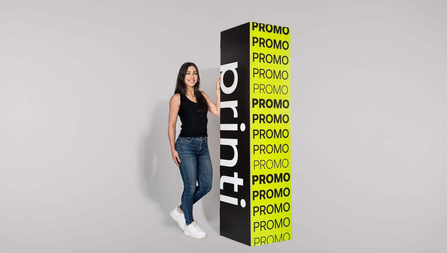 Mulher branca de cabelos lisos com regata preta, calça jeans skinny e tênis branco segurando totem quadriedro nas cores preto e verde-limão