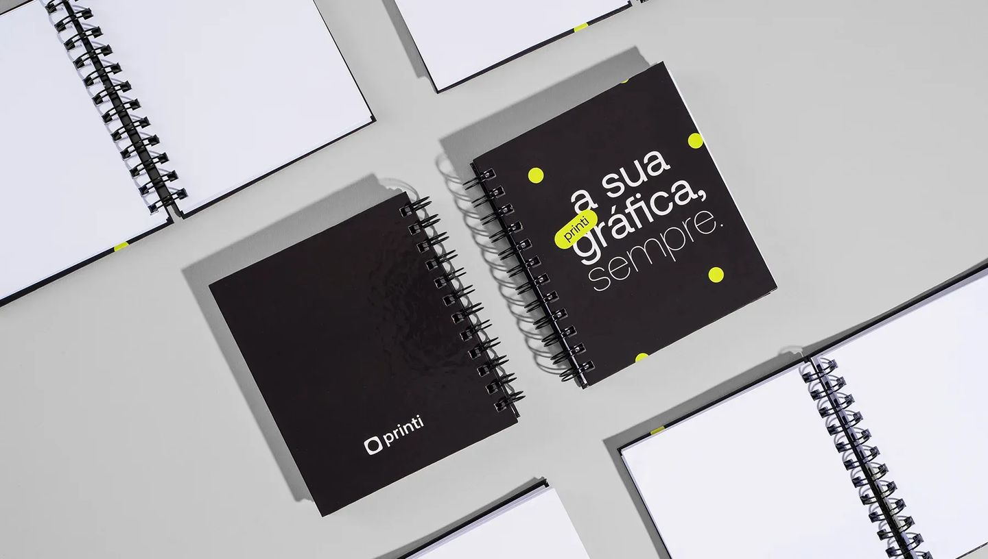Caderno pequeno personalizado da Printi com capa dura impressa em design moderno. A imagem destaca o acabamento em espiral wire-o preto e a nitidez da impressão personalizada, ideal para brindes corporativos.