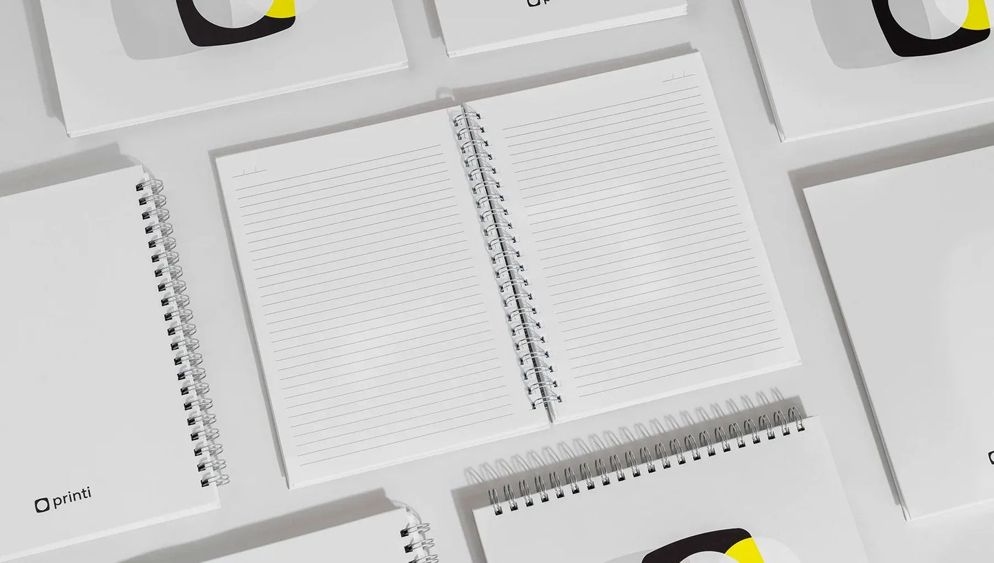 Visão interna de caderno personalizado Printi com páginas pautadas e acabamento em espiral wire-o prata, ideal para escrita e organização.