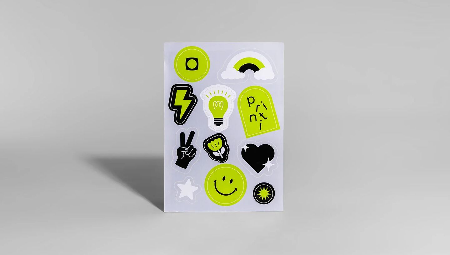 Detalhe de cartela de adesivos personalizados da Printi com a frase "A sua gráfica, sempre" e ícones coloridos em alta resolução.