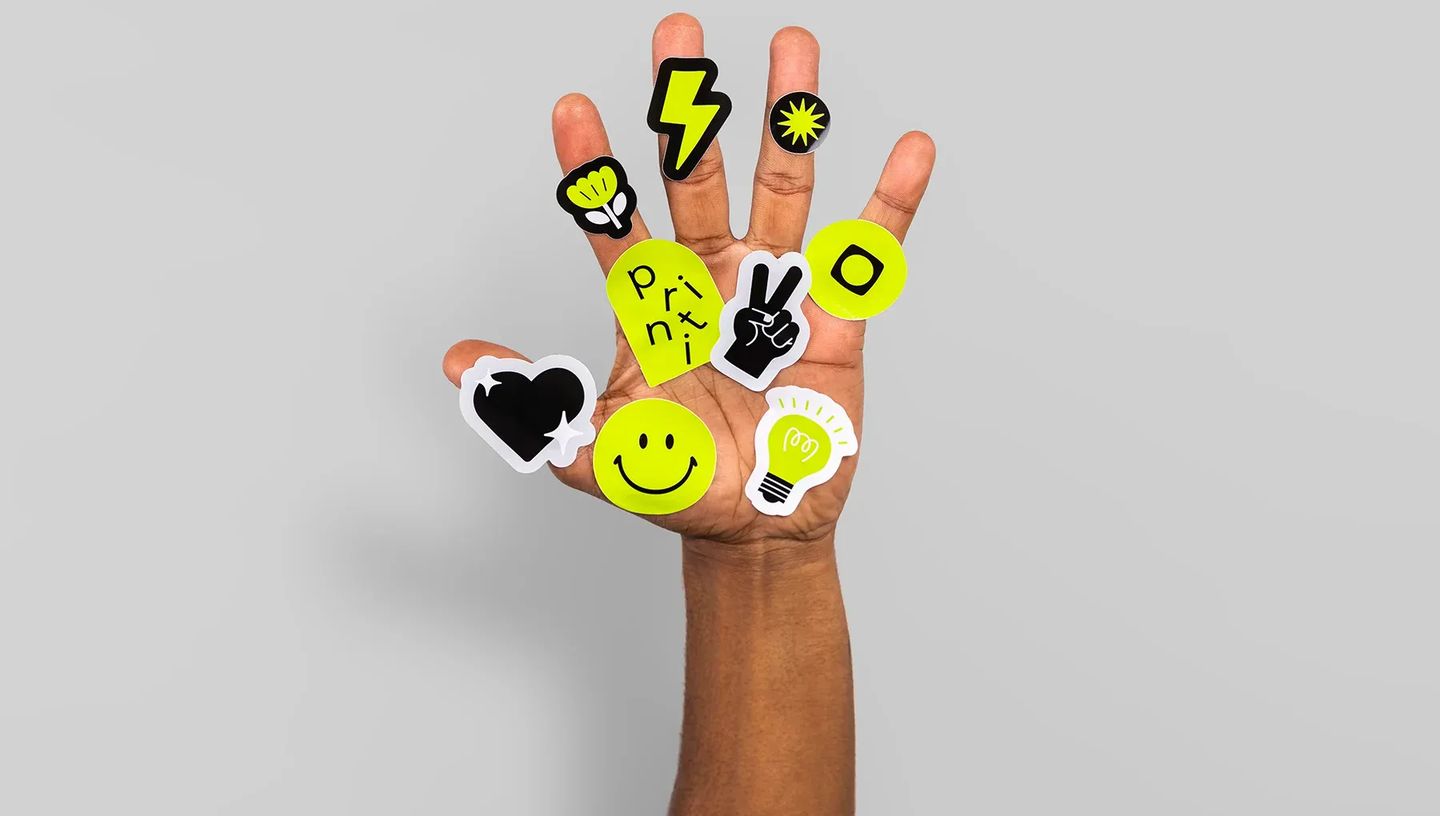 Mão destacando adesivo de raio verde neon de uma cartela personalizada da Printi, demonstrando o meio-corte e facilidade de uso.