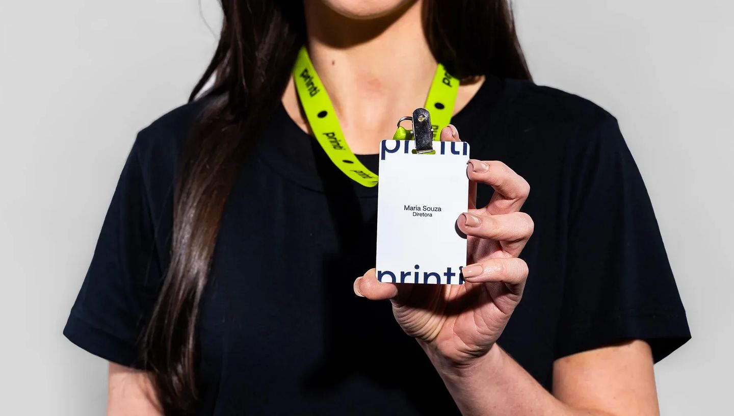 Mulher vestindo camiseta preta segurando um crachá personalizado da Printi com os dados Maria Souza Diretora e usando um cordão para crachá verde-limão.