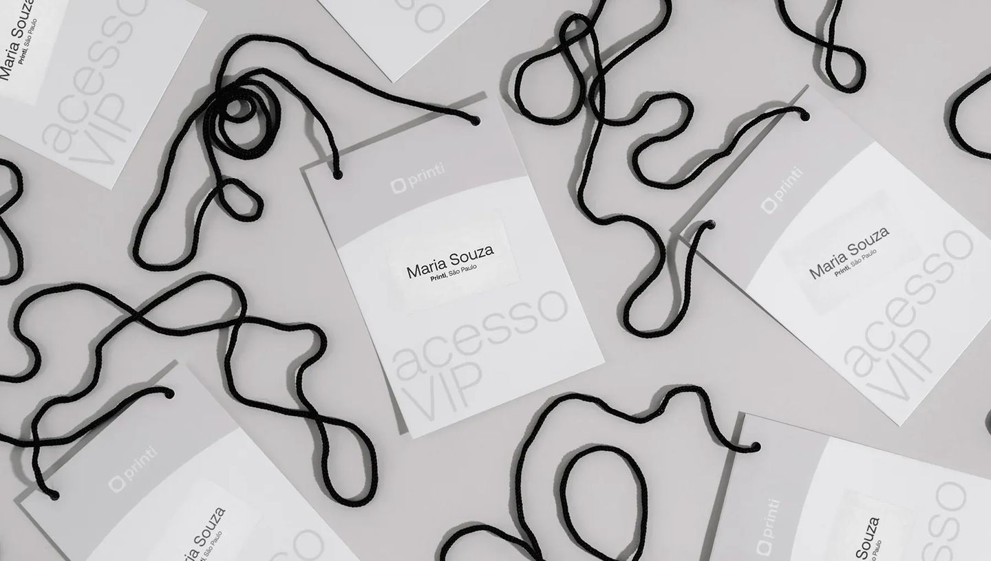 Vista superior de várias credenciais de identificação personalizadas espalhadas com cordões pretos. Os crachás de acesso VIP exibem o logotipo da Printi e o nome impresso "Maria Souza".