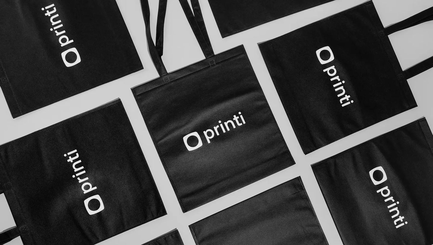 Modelos de sacola ecológica preta personalizada com o logotipo da Printi para brindes corporativos.