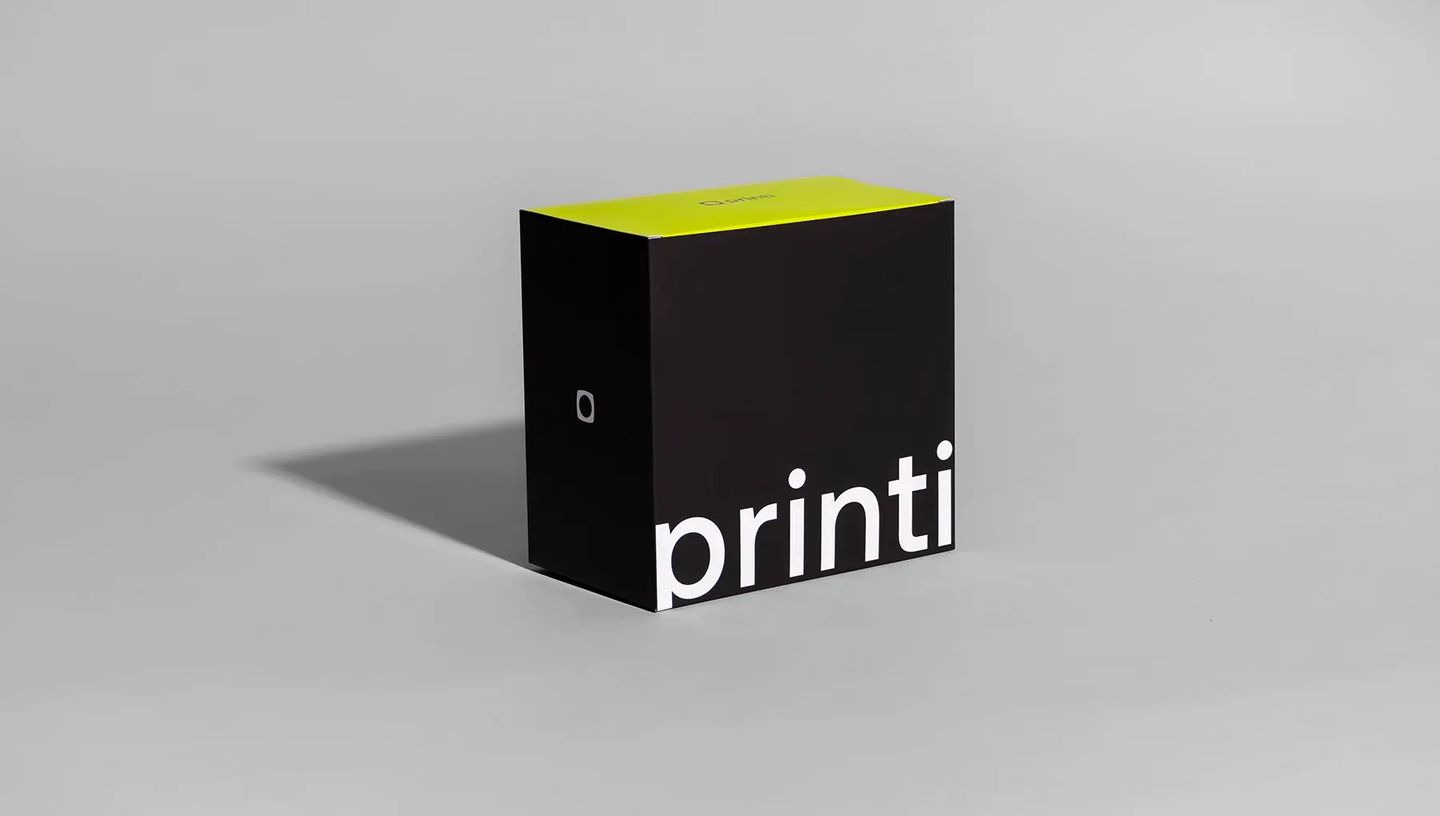 Embalagem personalizada da marca Printi nas cores preto e verde-limão, com logotipo branco, posicionada centralizada em um fundo neutro.